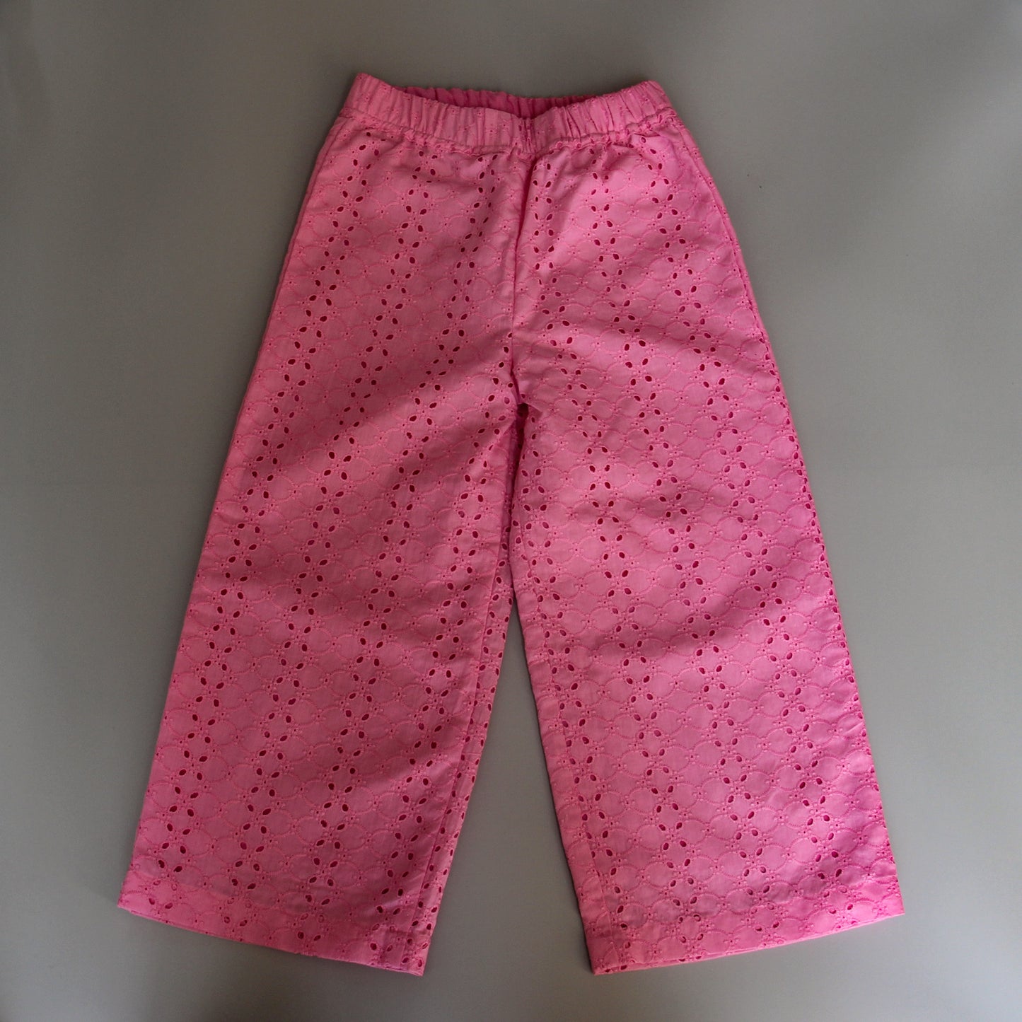 Pink pants with eyelet details on a gray background