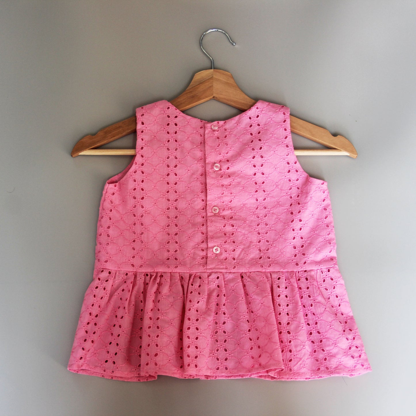Pink sleeveless top on a wooden hanger against a plain background