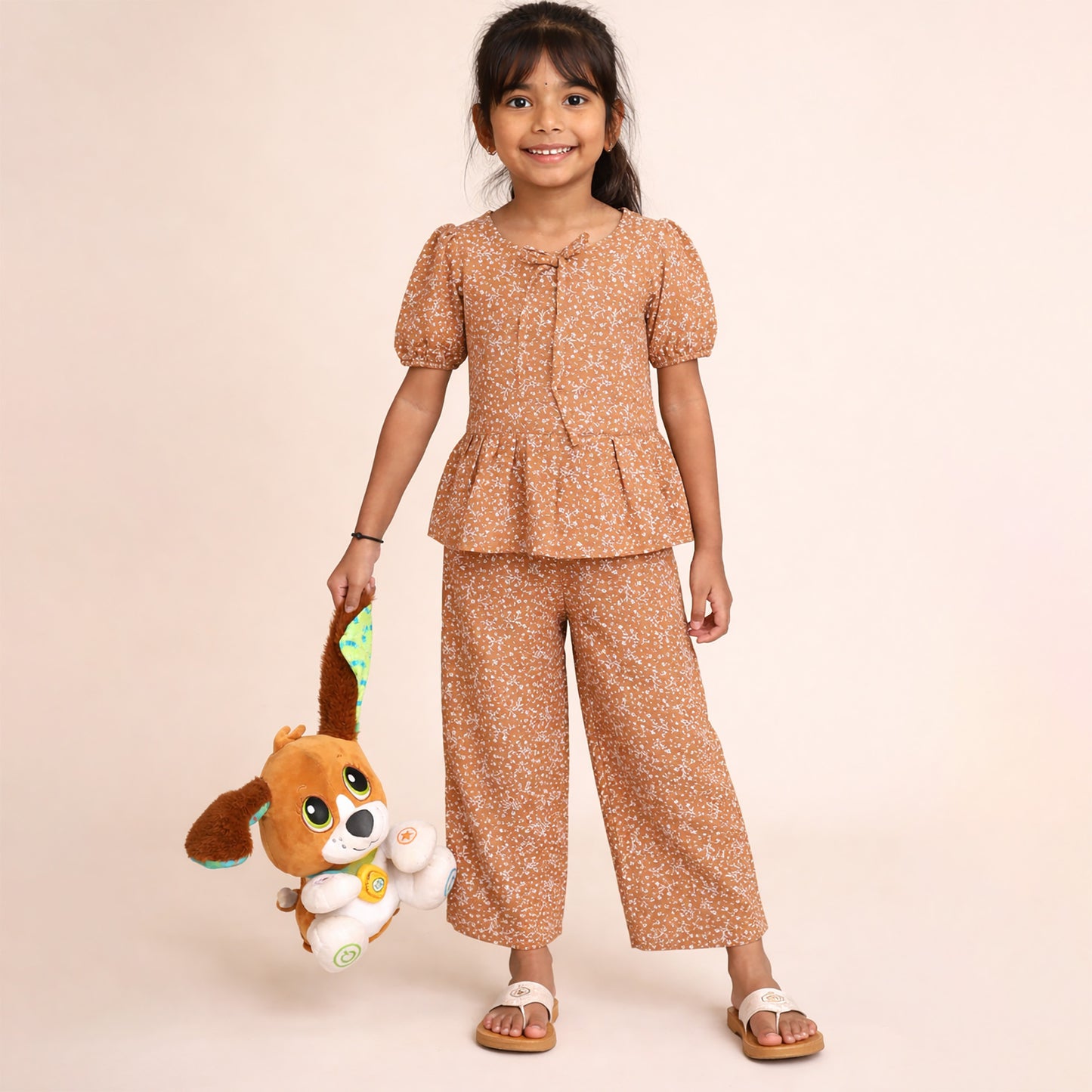 Young girl in a matching top and pants set holding a plush toy on a beige background