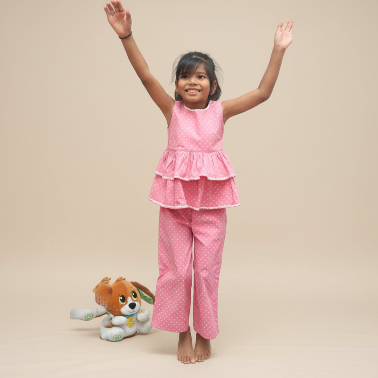 Child wearing a pink rose floral print outfit with arms raised on a plain background