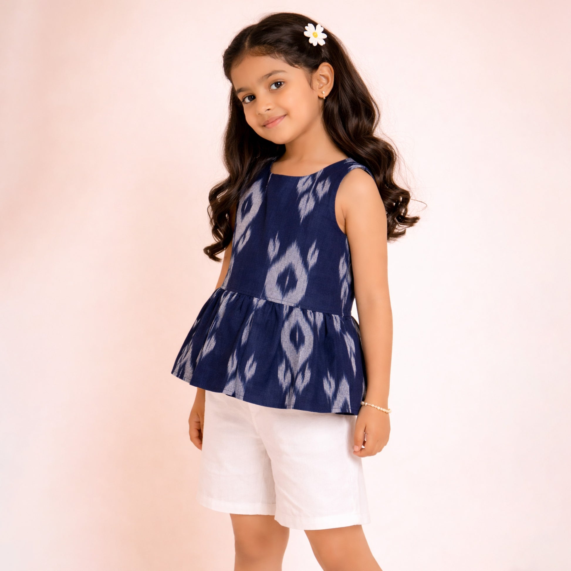 Young girl wearing a navy blue patterned top and white shorts on a light pink background