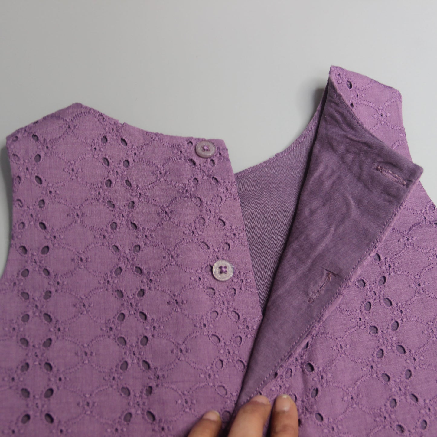 Purple lace garment with a hand touching the fabric on a light gray background