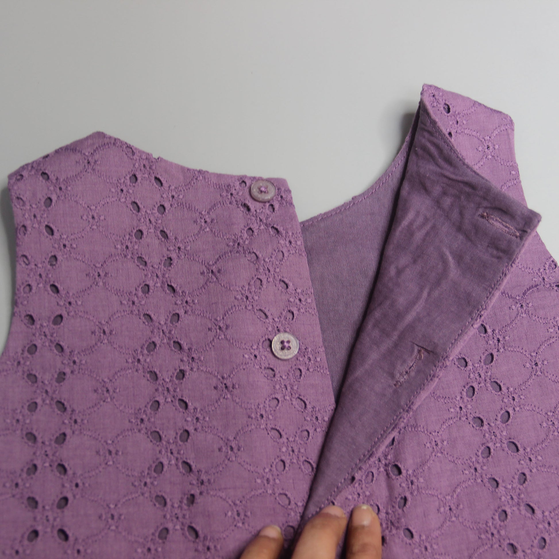 Purple lace garment with a hand touching the fabric on a light gray background